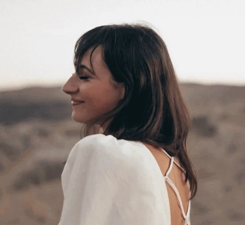 A woman in a white top looking back over her shoulder and smiling, open ground behind her