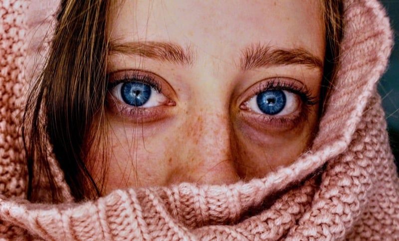 A close-up of a woman with freckles wrapped in a pink knitted scarf