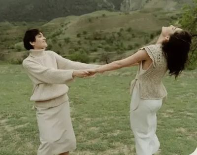 Two women holding both hands and leaning back, turning together in a green valley