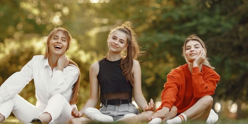 Three teenage girls sitting together on the grass in a park, laughing