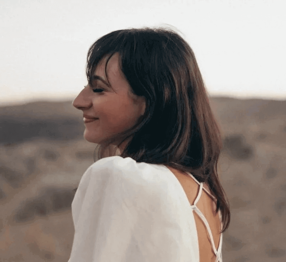 A woman in a white top looking back over her shoulder and smiling, open ground behind her