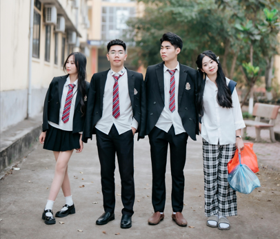Four teenagers in school uniform standing together on a path outside a school building