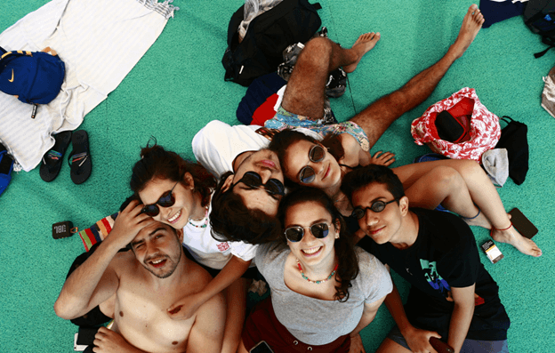 Six friends in sunglasses lying in a circle on green ground, photographed from above