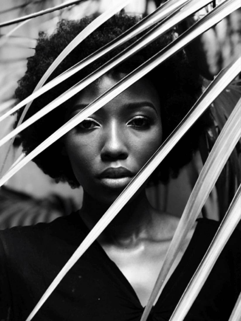 A woman standing among tall leaves, looking toward the camera