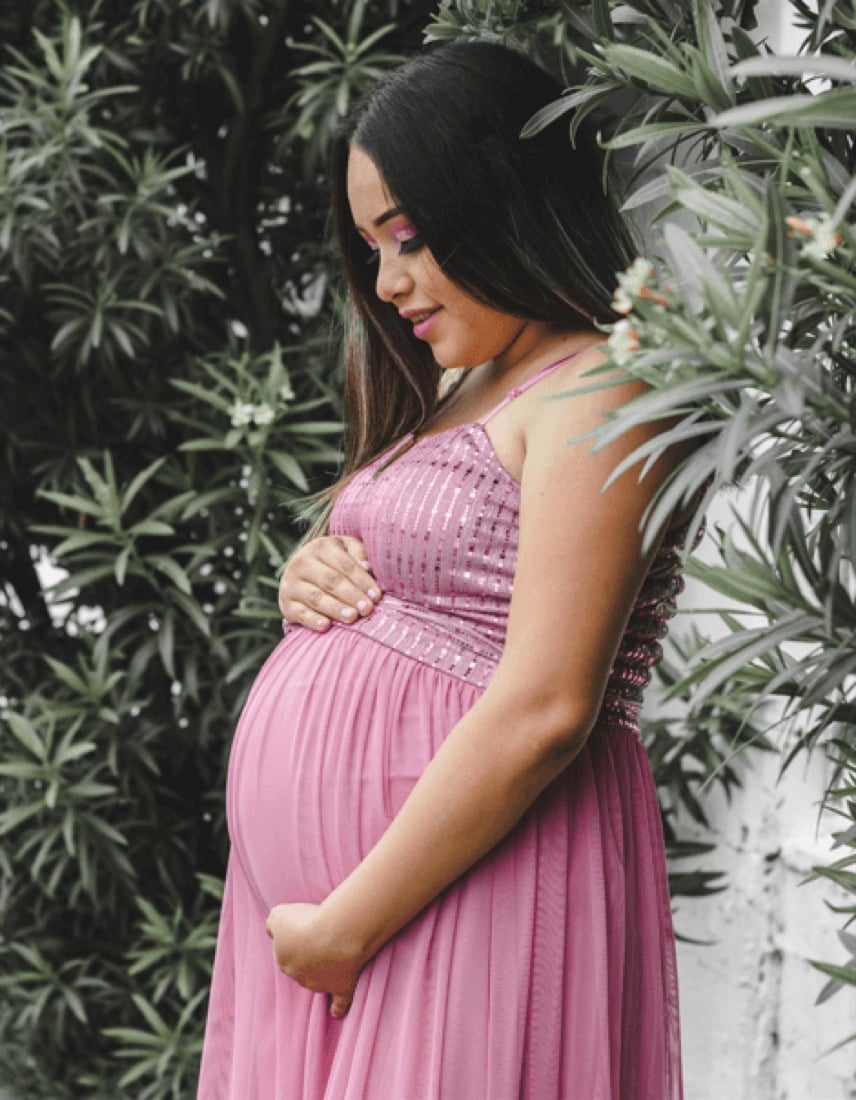 A pregnant woman standing outdoors with her hands resting on her bump