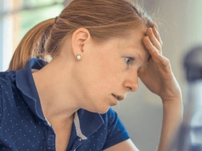 A woman resting her forehead on her hand, looking down