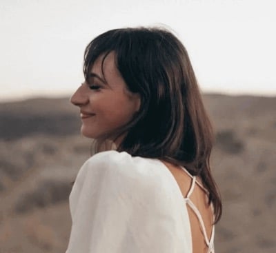 A woman in a white top looking back over her shoulder and smiling, open ground behind her