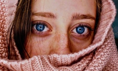 A close-up of a woman with freckles wrapped in a pink knitted scarf