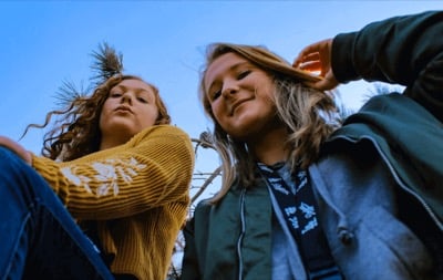 Two teenage girls photographed from below against a clear blue sky