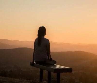 The silhouette of a woman on a bench watching the sun set over hills