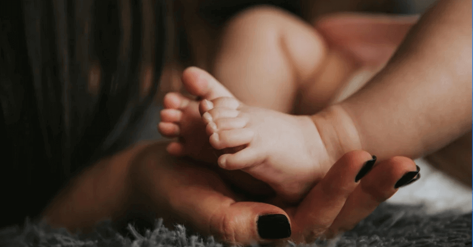 A baby’s bare feet cradled in a parent’s hand over a shag rug