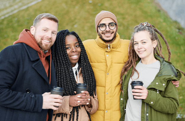 Four friends holding coffee cups, smiling together outdoors