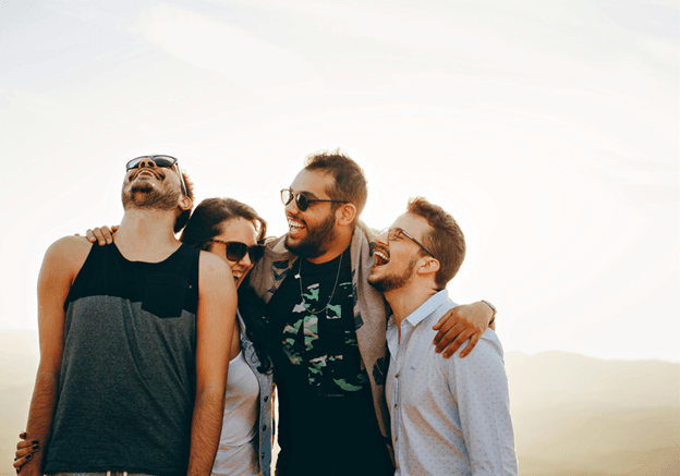 Four friends laughing together against a bright sky