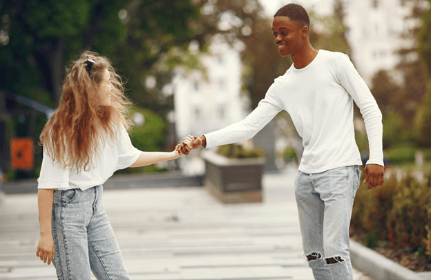 Two teenagers in white tops walking hand in hand along a paved path lined with trees